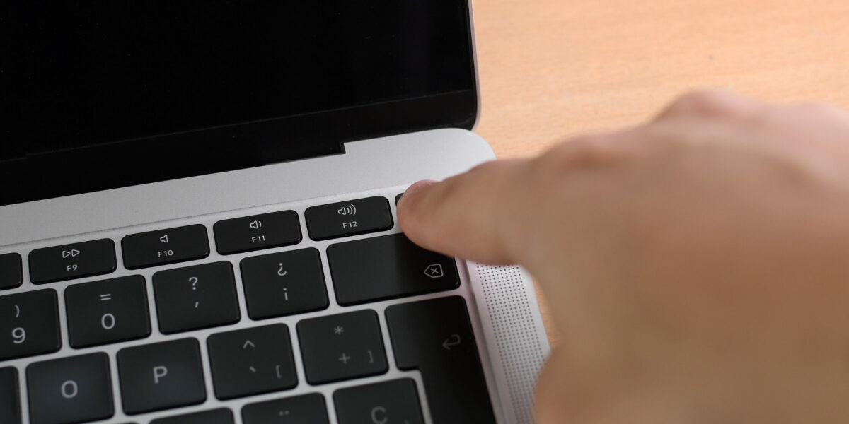 Hand is pressing power on key on laptop computer, close up. Finger presses power button to turn on laptop. Man is pushing laptop power button